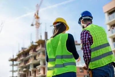 Two people in yellow vests and hard hats standing on a construction site.