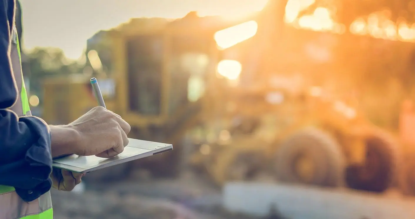 A person is typing on a laptop in front of a construction site.